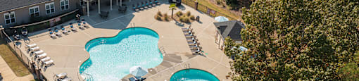 A large outdoor swimming pool surrounded by a fence and lounge chairs.