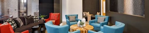 A modern living room with a mix of red and blue chairs and a wooden ceiling.