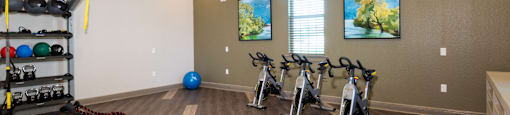 a fitness room with exercise bikes and weights on a wooden floor