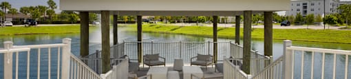 A gazebo with a white roof is surrounded by a white fence and has a deck with chairs and a table.