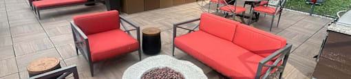 A wooden table with a fire pit in the middle of a patio with red couches.