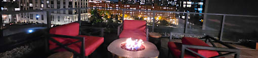 A fire pit sits in the middle of a wooden table on a rooftop patio.