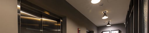 A hallway with a metal elevator on the left and a wall with pictures on the right.