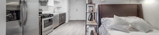 A modern kitchen with stainless steel appliances and a bed with a brown headboard.