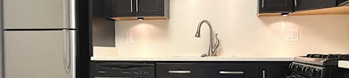 A kitchen with black cabinets and a stainless steel refrigerator.