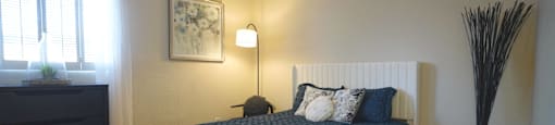 A bedroom with a blue bedspread and a black floor lamp.