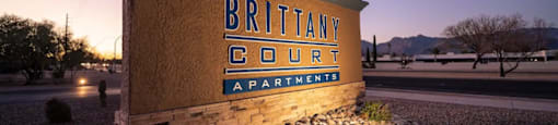 A wooden sign that says Brittany Court Apartments is in front of a street lamp.