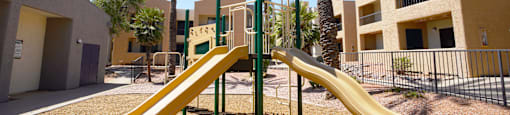 A playground with a yellow slide and palm trees.