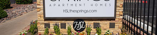 The sign for The Springs Apartment Homes is displayed in front of a fence.