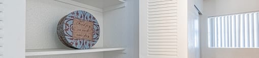 A small room with a white shelf and a round decorative plate on it.