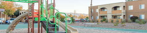 A playground with a green slide and a sandbox.