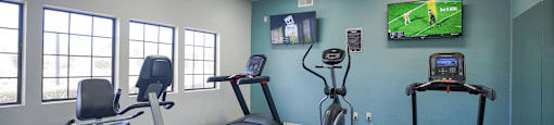 A gym with treadmills, exercise bikes, and a television playing a soccer game.