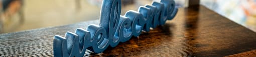 A blue 3D printed word "welcome" on a wooden surface.