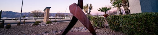 A large metal sculpture of a woman is in the foreground of a gravel area.