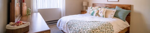 A bedroom with a bed, nightstand, and a window with blinds.