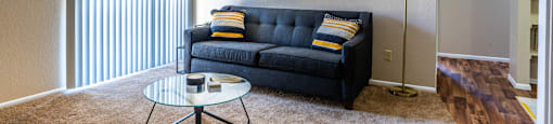 A living room with a black couch and a glass coffee table.