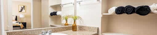 A bathroom with a sink, mirror, and shelves with towels.