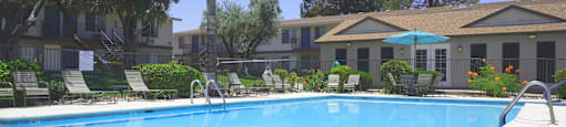 A swimming pool surrounded by chairs and trees.