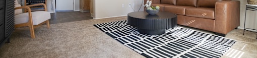 A living room with a brown couch and a black and white rug.