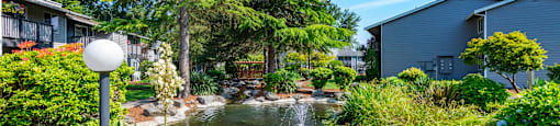 a garden with a pond and trees in front of houses