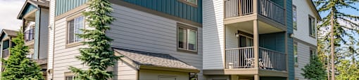 the view of two story apartment buildings with balconies and trees