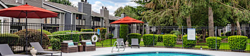 a swimming pool with umbrellas and chairs in front of apartment buildings