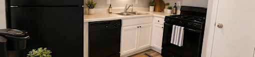 A black fridge and oven in a kitchen with white cabinets.