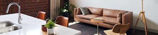 A modern kitchen with a white countertop and brown leather couch.