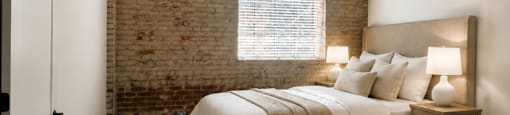 A bedroom with a bed, nightstand, and a window with blinds.