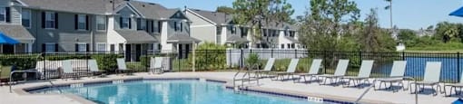 a resort style pool with chaise lounge chairs and apartment buildings in the background