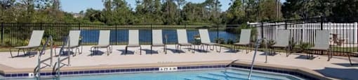 a swimming pool with chaise lounge chairs and trees in the background