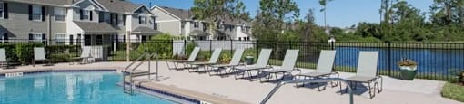 a swimming pool with chaise lounge chairs in front of a row of houses