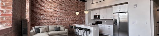 A modern kitchen and living room with a brick wall.