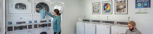 A man is sitting on a chair reading a book in a room with washing machines.