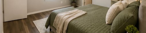 A bedroom with a bed, a plant, and a shelf with decorative items.
