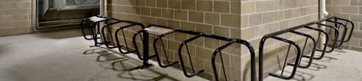 A row of black bicycle racks are lined up against a wall with a row of air conditioning units above them.
