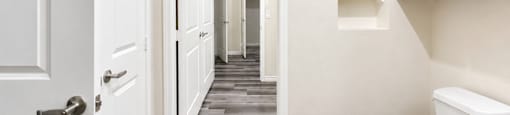 A white toilet sits in a hallway with a white door on the left.
