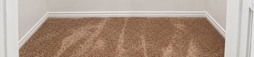 A white wall with a brown carpet and a brown shelf.
