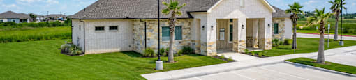 A house with a grey roof and white walls is surrounded by a green lawn.