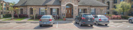 A parking lot with several cars parked in front of a building with a stone facade and a large arched doorway.