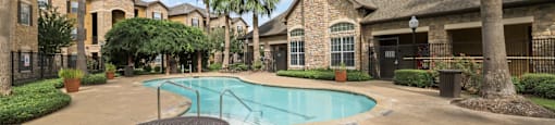 A pool surrounded by palm trees and a brick house.