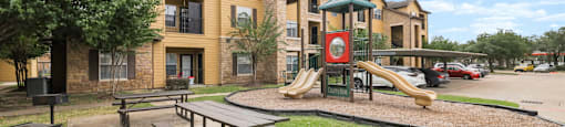 A playground with a slide and a picnic table in front of apartment buildings.