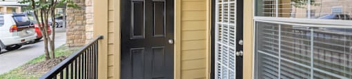 A black door is on the left side of a tan building.