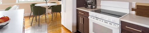 a kitchen with brown cabinets and white appliances and a table with chairs at Beverly Village for Living & the Arts Apartments, Massachusetts
