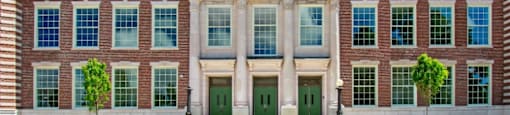 a large brick building with green doors and white columns at Beverly Village for Living & the Arts Apartments, Beverly, 01915