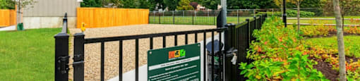 a gate with a sign on it in front of a garden at Beverly Village for Living & the Arts Apartments, Beverly, 01915