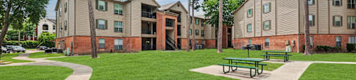 A grassy area in front of apartment buildings with benches.