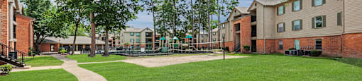 A grassy area with a concrete walkway and apartment buildings in the background.