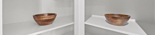 Two wooden bowls on shelves in a white refrigerator.