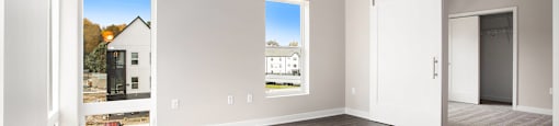 A spacious room with a ceiling fan and two windows.